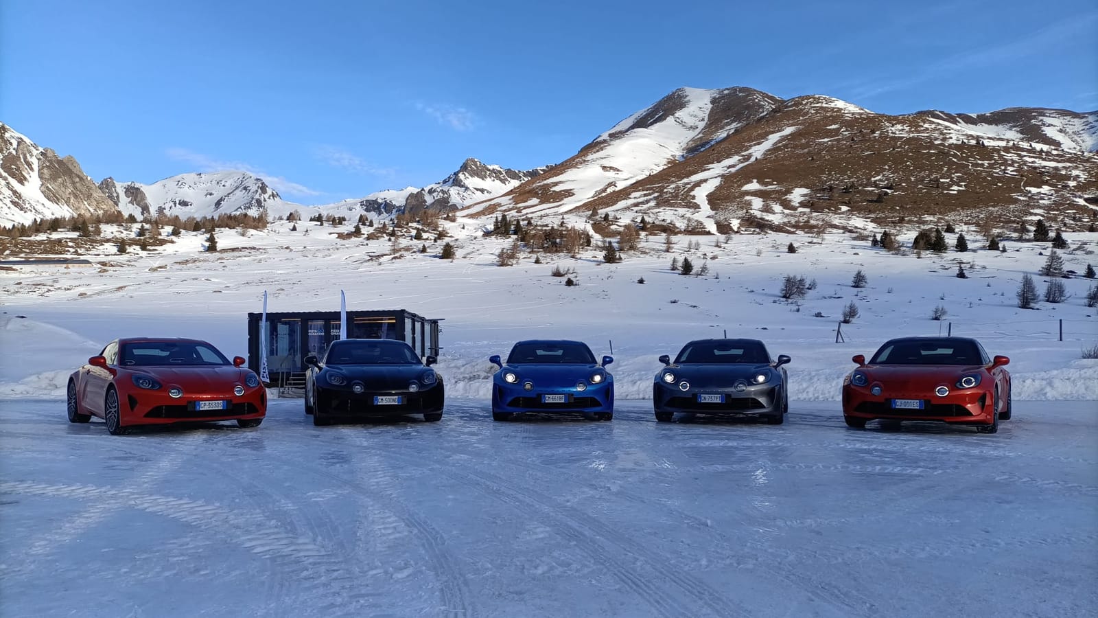 Cinque Alpine A110 allineate sulla neve, con le montagne sullo sfondo, all'evento Alpine ICE Driving